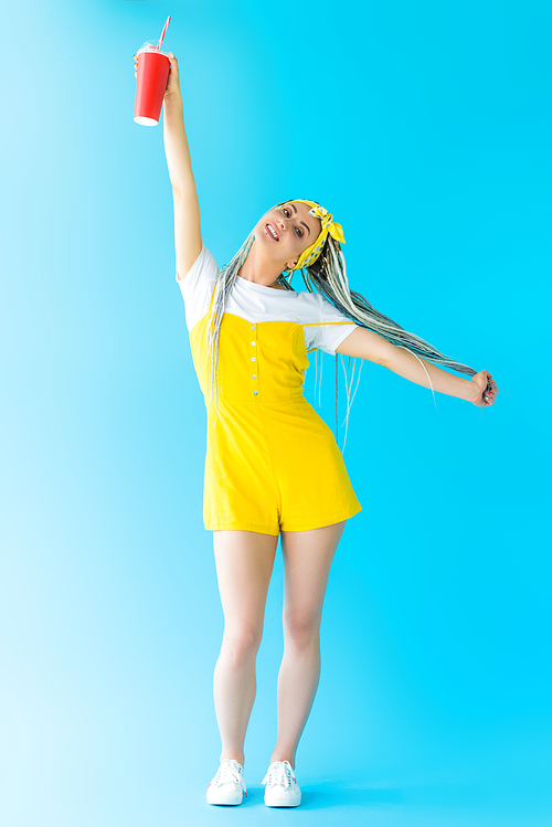 beautiful happy girl with dreadlocks and soda drink posing with outstretched hands on turquoise