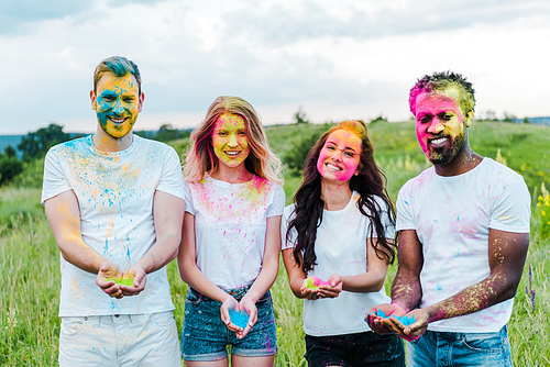 happy multicultural friends holding colorful holi paints in hands