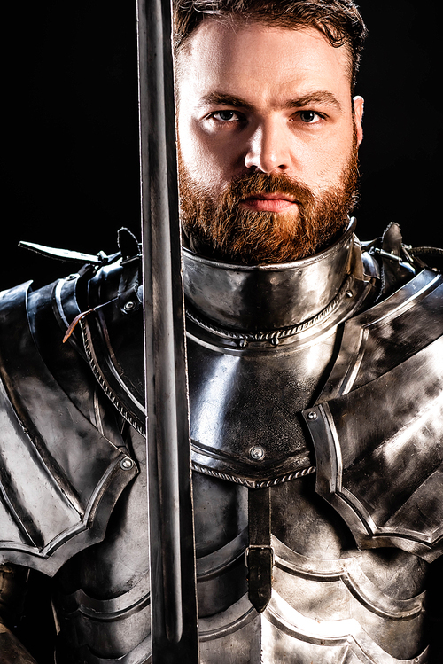 handsome knight in armor holding sword isolated on black