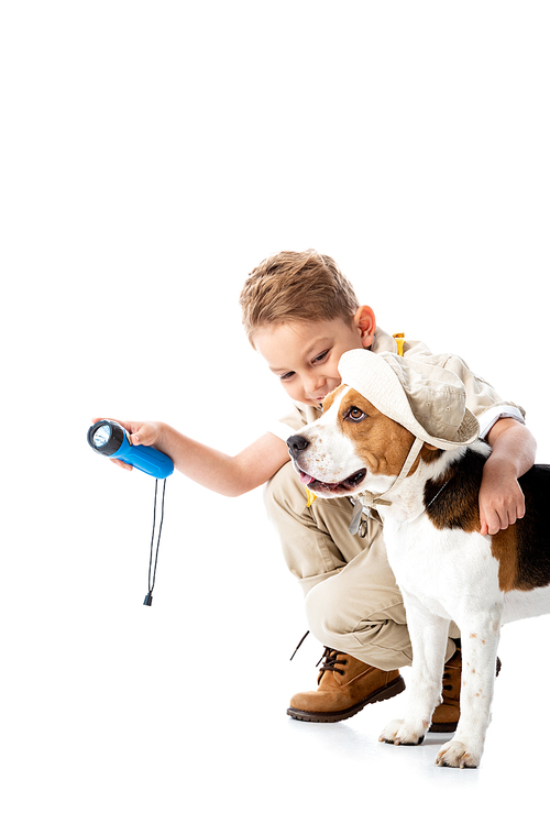 smiling explorer child holding flashlight and embracing beagle dog in hat on white