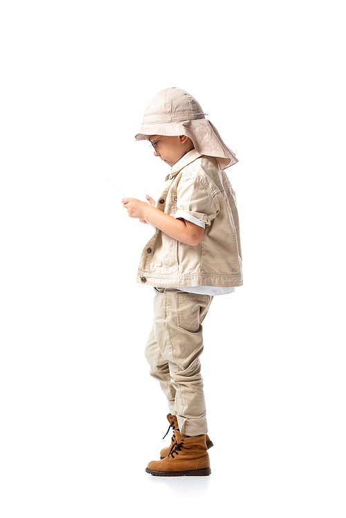 side view of explorer child in glasses and hat using digital tablet isolated on white