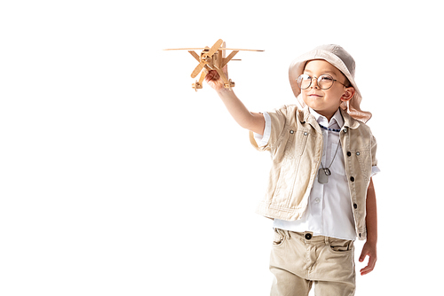 smiling explorer boy in glasses and hat holding wooden toy plane isolated on white