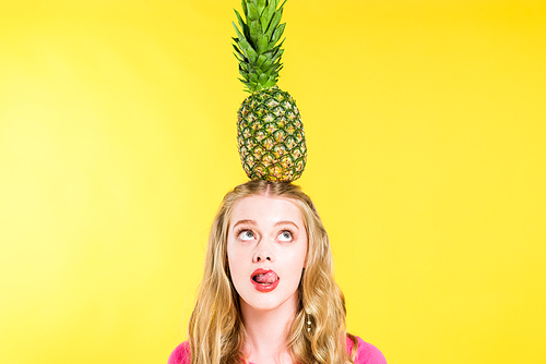 beautiful girl posing with pineapple on head and sticking tongue out Isolated On yellow