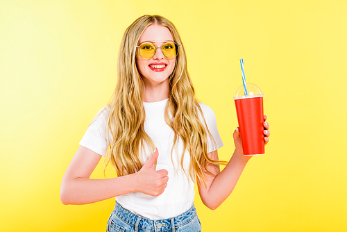 beautiful girl in sunglasses with drink in disposable cup doing thumb up On yellow