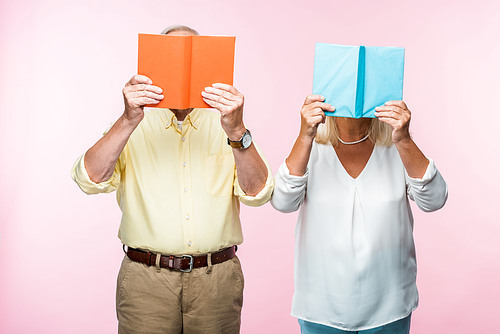 couple of pensioners standing and covering faces with books isolated on pink