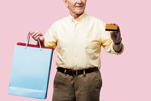 cropped view of happy retired man holding credit card and shopping bags isolated on pink