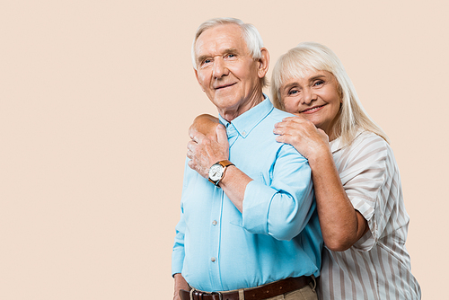 cheerful retired woman hugging senior husband isolated on beige