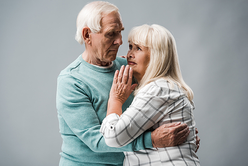 senior man with grey hair hugging upset wife on grey