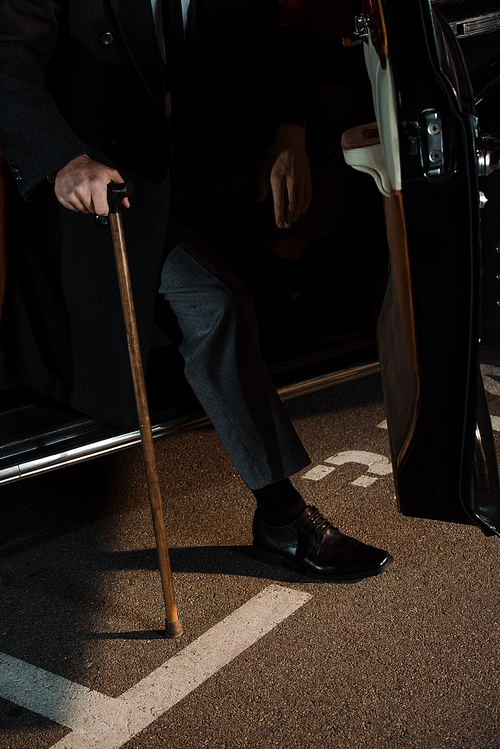 cropped view of gangster holding walking cane near retro car with opened car door
