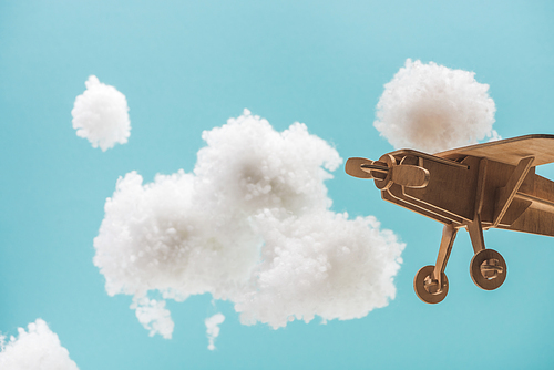 wooden toy plane flying among white fluffy clouds made of cotton wool isolated on blue