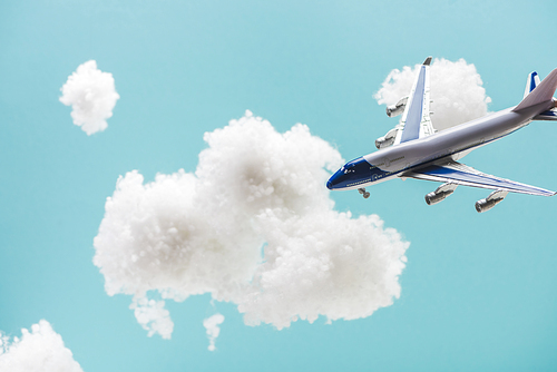 toy plane flying among white fluffy clouds made of cotton wool isolated on blue