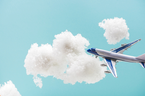 toy plane flying among white fluffy clouds made of cotton wool isolated on blue