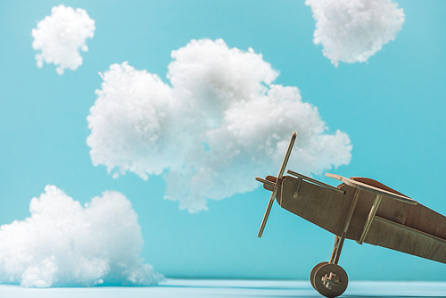 wooden toy plane among white fluffy clouds made of cotton wool isolated on blue