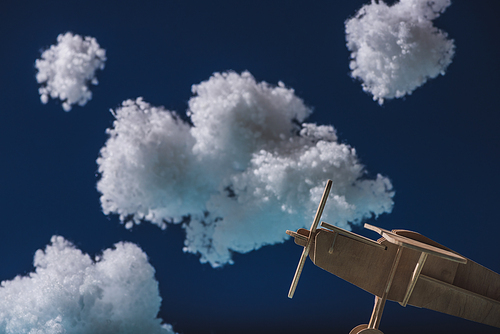 wooden toy plane flying among white fluffy clouds made of cotton wool isolated on dark blue
