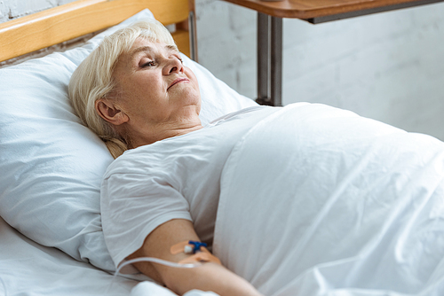 sick senior woman with grey hair on bed in clinic