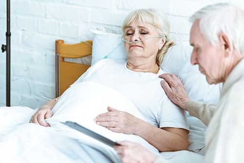 senior man holding clipboard with sick wife in clinic