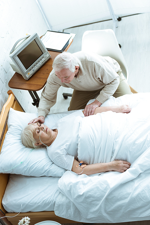 overhead view of senior man stroking wife in coma in clinic