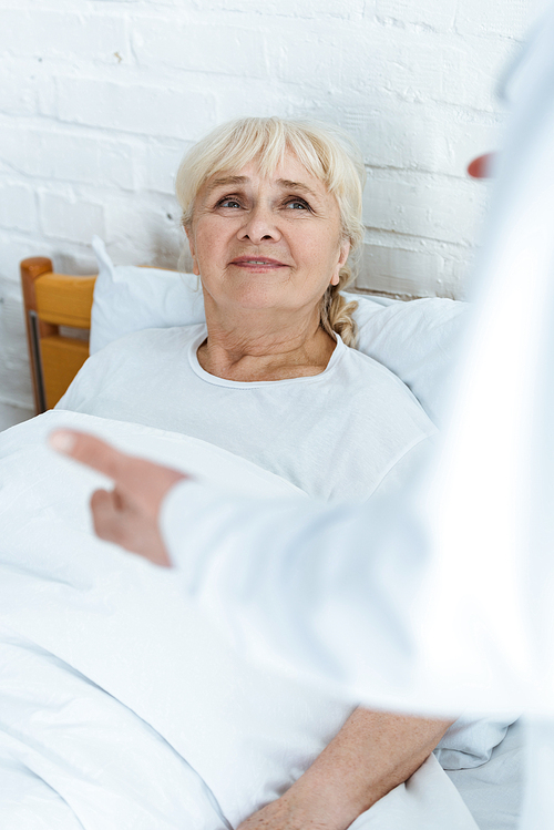 partial view of doctor in white coat and senior patient in clinic