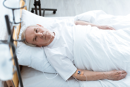 overhead view of sick senior man lying on bed in clinic