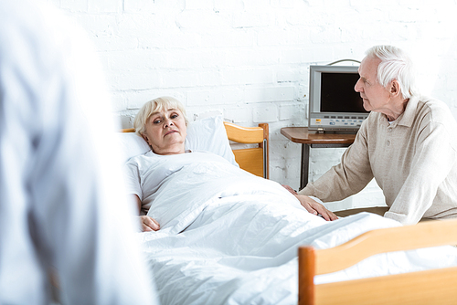 partial view of doctor in white coat, sick patient and senior man in hospital