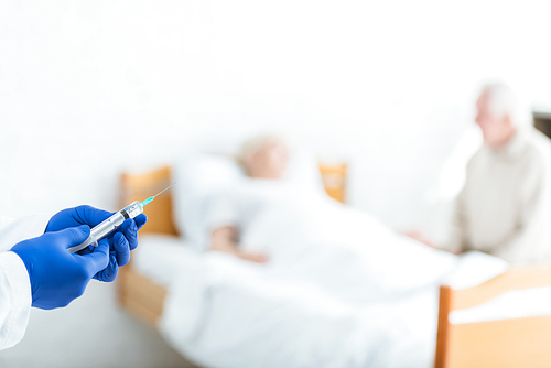 partial view of doctor in latex gloves holding syringe, ill patient and senior man in clinic