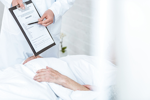 partial view of doctor holding clipboard and pen and ill patient in clinic