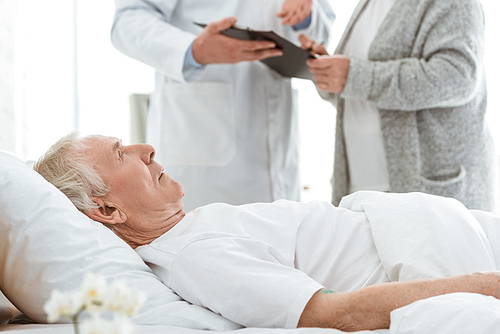 partial view of doctor holding clipboard, sick patient and senior woman in clinic