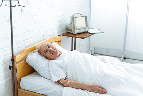 smiling ill senior man lying on bed in clinic