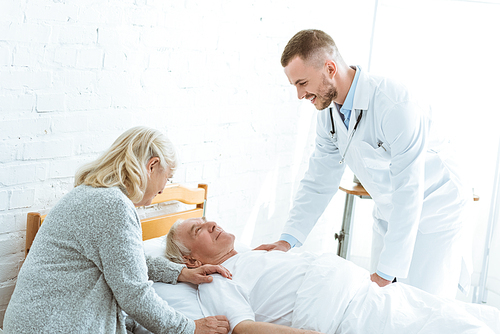 smiling doctor and senior woman near ill patient in clinic