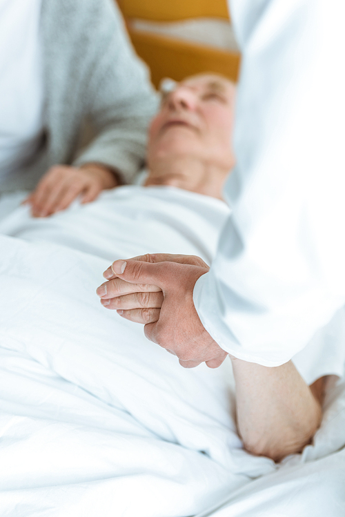 cropped view of doctor standing near patient in coma and holding his hand