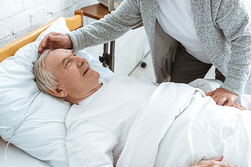 partial view of senior woman stroking sick smiling husbend in clinic