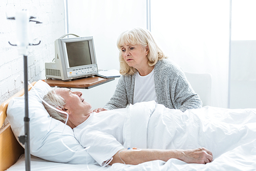 worried senior woman looking at ill husbend in hospital