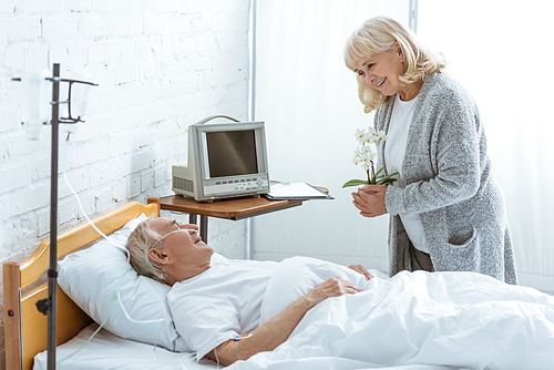 smiling senior woman with orchids and sick patient in hospital