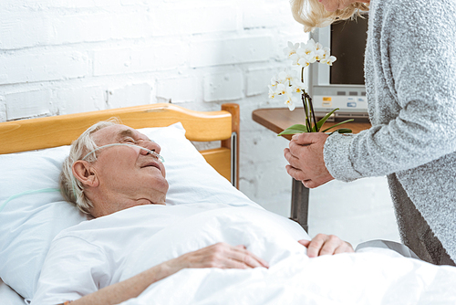 cropped view of senior woman with orchids and sick patient in hospital