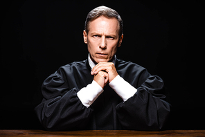 judge in judicial robe sitting at table and  isolated on black