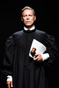 judge in judicial robe holding gavel and papers isolated on black