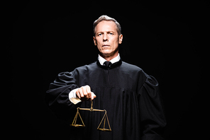 judge in judicial robe holding scales of justice isolated on black