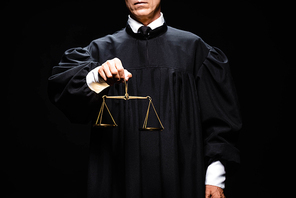 cropped view of judge in judicial robe holding scales of justice isolated on black