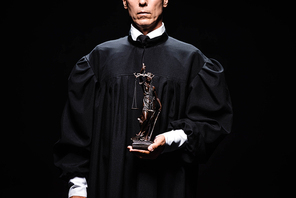 cropped view of judge in judicial robe holding themis figure isolated on black