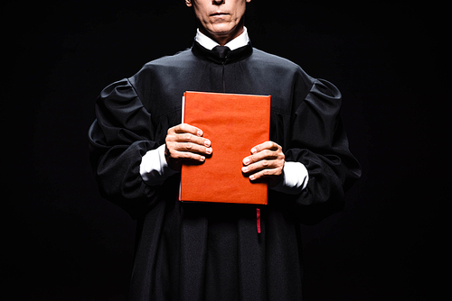 cropped view of judge in judicial robe holding orange book isolated on black