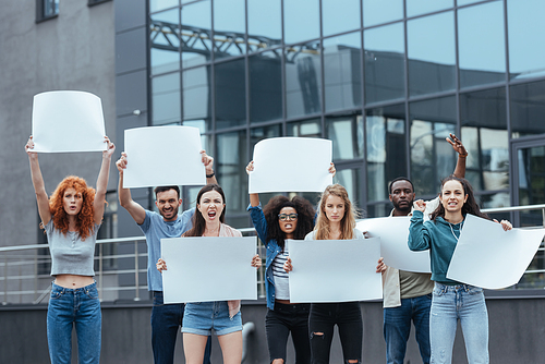 emotional multicultural people standing with blank placards near building