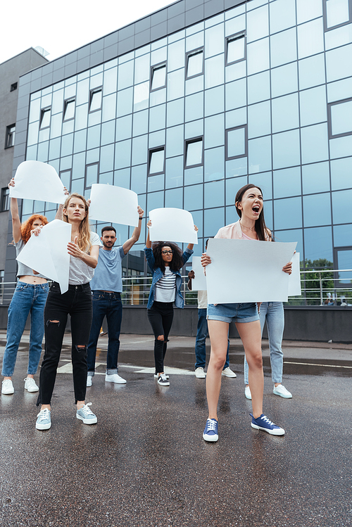 emotional multicultural people with blank placards near building