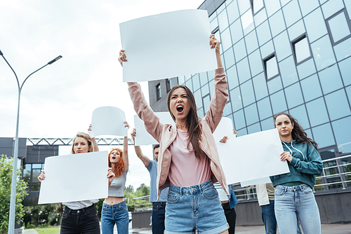 selective focus of emotional girl holding blank placard and screaming near men and women