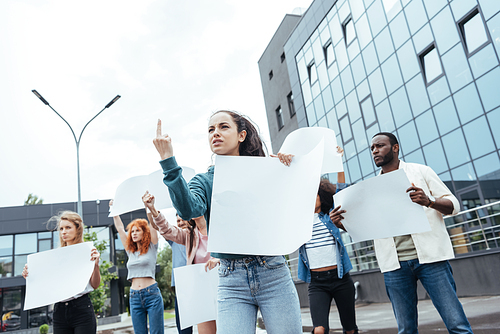 low angle view of girl showing middle finger while holding empty board near multicultural people