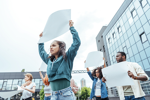 selective focus of girl holding empty board near multicultural people