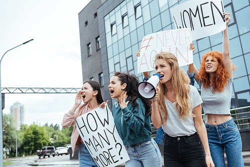 selective focus of girl holding megaphone and screaming near multicultural women on meeting