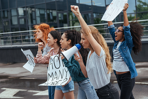 selective focus of girl gesturing while holding megaphone near multicultural women on meeting