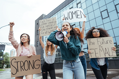 selective focus of emotional girl holding megaphone and screaming near multicultural women holding placards on meeting