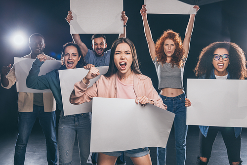 young emotional multicultural people screaming while holding blank placards on black