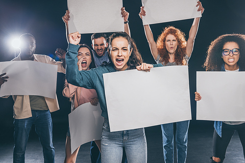 emotional multicultural people screaming while holding blank placards on black